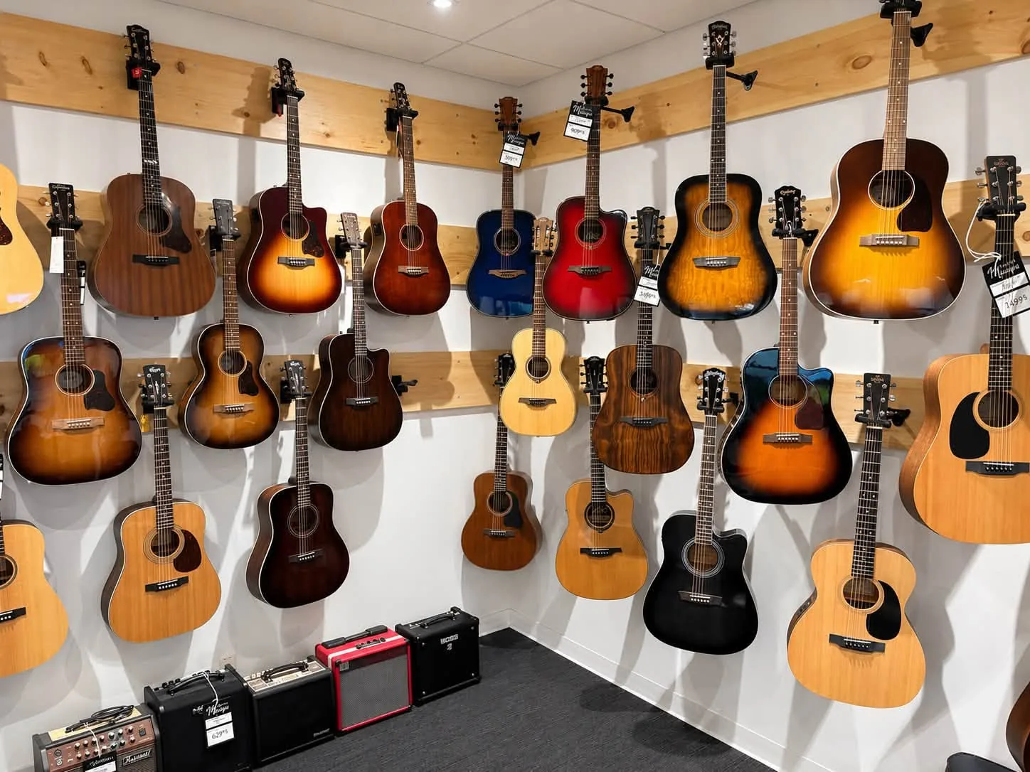 Mur d’une trentaine de guitares acoustiques accrochées avec leurs étiquettes de prix, au-dessus d’une rangée d’amplis, dans le magasin Multi Musique.