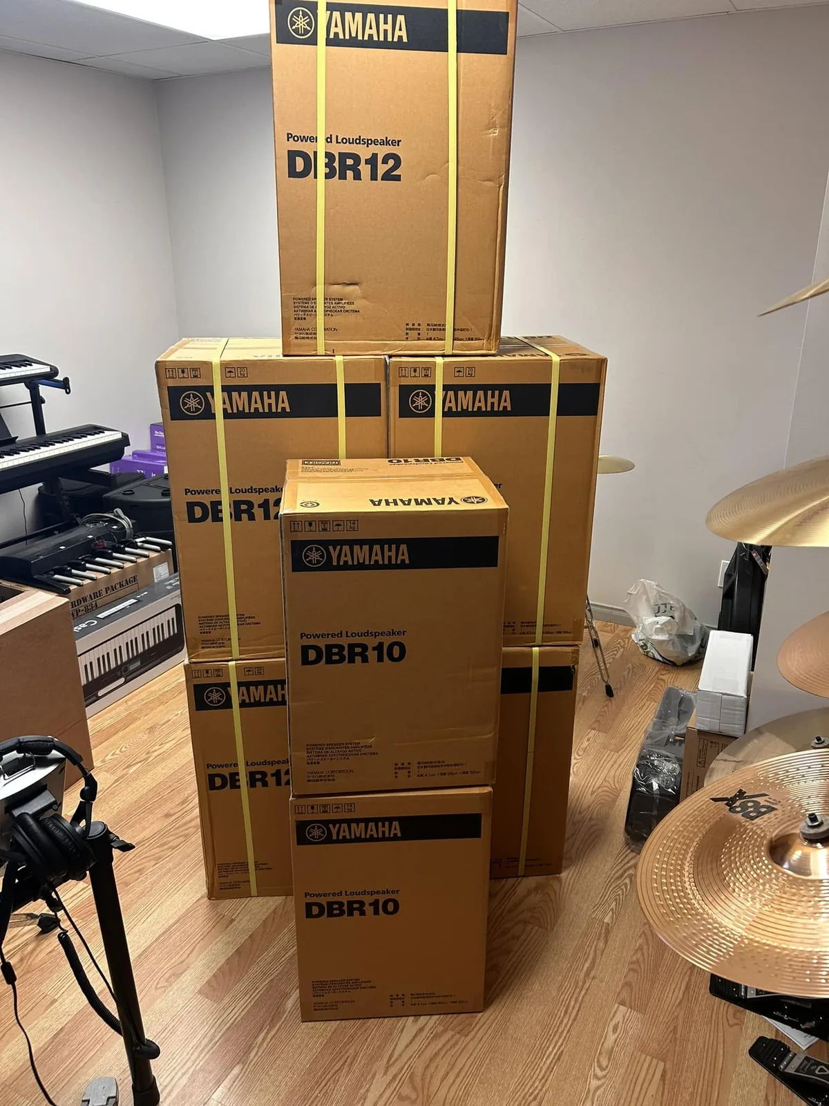Pile de boîtes de haut-parleurs amplifiés Yamaha DBR10 et DBR12 dans l’arrière-magasin, à côté d’un clavier et de cymbales.